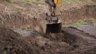Kazı kazıcı kir yığınının üzerine atlıyor ve temizliyor. Vinçteki maşa inşaat malzemeleri taşıyor. Gevşek maddeler. Ormanın arka planı