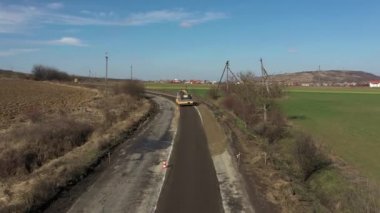Paver Nakliyecisi 'nin yeni yapılmış düz bir yolda fırlatılıp düzleştirilirken havadan drone görüntüsü. Asfalt kaldıracı tamir edilen şehir yoluna asfalt uyguluyor
