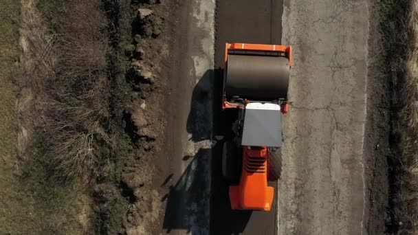 Aerial drone shot of Paver mover on a flat newly made road, ramming and leveling. Aserradero de asfalto aplicando asfalto en la carretera de la ciudad reparada — Vídeo de stock