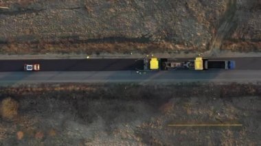Paver Nakliyecisi 'nin yeni yapılmış düz bir yolda fırlatılıp düzleştirilirken havadan drone görüntüsü. Asfalt kaldıracı tamir edilen şehir yoluna asfalt uyguluyor
