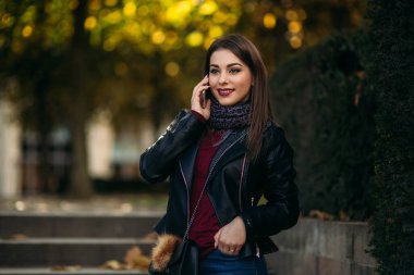 Siyah çantalı ve bordo bluzlu siyah ceketli şık bir bayan. Çekici genç bayan telefonda konuşuyor.