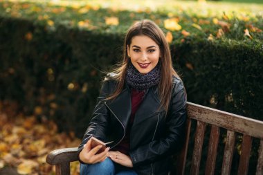 Siyah çantalı ve bordo bluzlu siyah ceketli şık bir bayan. Çekici genç kadın telefon kullanıyor.