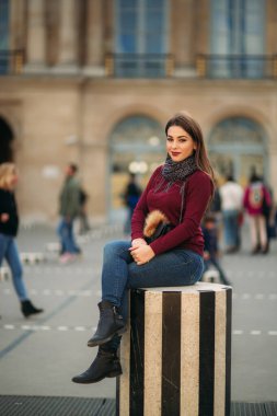 Gri eşarplı bordo bluzlu çekici genç kadın çizgili kürsünün üzerinde oturuyor. Paris 'te mutlu bir kadın