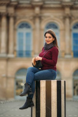 Gri eşarplı bordo bluzlu çekici genç kadın çizgili kürsünün üzerinde oturuyor. Paris 'te mutlu bir kadın