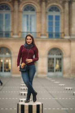 Çizgili kürsünün üzerinde gri eşarp standı olan bordo bluzlu çekici genç bir kadın. Paris 'te mutlu bir kadın