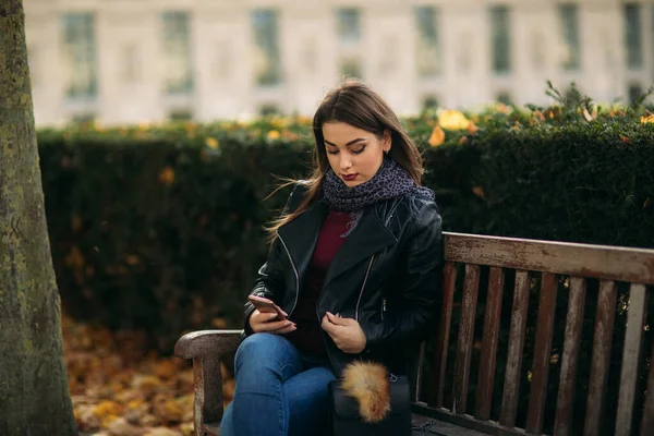 Stijlvolle mooie dame in een zwart leren jasje met een zwarte tas en bordeaux blouse. Aantrekkelijke jonge vrouw gebruik telefoon — Stockfoto