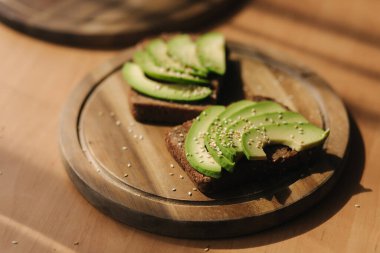 Avokado sandviçi ve çavdar ekmeği. Yukarıdan taze kesilmiş avokadolarla yapılmış. Tahtanın üzerine susam tohumları serpiştirilmiş vejetaryen sandviç.