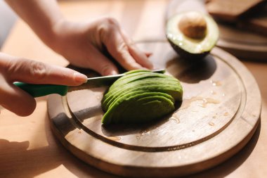 Evdeki ahşap tahtada avokado dilimleyen kadına yakın çekim. Vejetaryen gıda konsepti