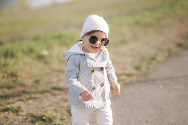둑 근처 공원을 걷고 있는 귀여운 여자 애. 선글라스를 쓴 예쁘고 귀여운 아가씨 — 스톡 사진