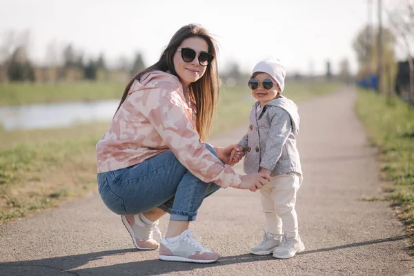 Happy little girl walk with her mother in park. Mom and daughter walk near promenade in Mothers Day. Cute little girl in sunglasses. Daughter hug mom. One and half year girl — Stock Photo, Image