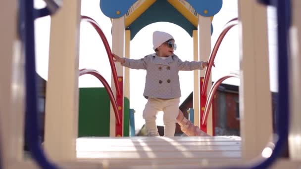 Schattig klein meisje lopen in de speeltuin en veel plezier. Schattig meisje in stijlvolle kleren — Stockvideo