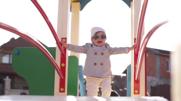 Милая маленькая девочка ходить по детской площадке и веселиться. Красивая девушка в стильной одежде — стоковое видео