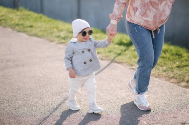 Küçük mutlu kız annesiyle parkta yürüyor. Anne ve kızı Anneler Günü 'nde gezinti güvertesine yakın yürüyorlar. Güneş gözlüklü şirin küçük kız.