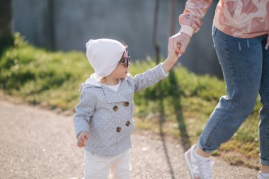 Küçük mutlu kız annesiyle parkta yürüyor. Anne ve kızı Anneler Günü 'nde gezinti güvertesine yakın yürüyorlar. Güneş gözlüklü şirin küçük kız.