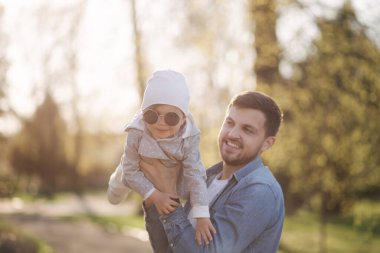 Babasının elinde mutlu şirin bir kız. Baba ve kızı parkta yürüyor. Aile havası. Biraz gül.