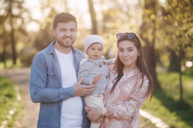 Parktaki mutlu aile portresi. Baba, anne ve küçük kız. Anne ve babasıyla çok sevimli. Genç bir aile, yakışıklı bir baba ve çekici genç bir anne. Anneler Günün kutlu olsun.