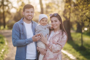Parktaki mutlu aile portresi. Baba, anne ve küçük kız. Anne ve babasıyla çok sevimli. Genç bir aile, yakışıklı bir baba ve çekici genç bir anne. Anneler Günün kutlu olsun.
