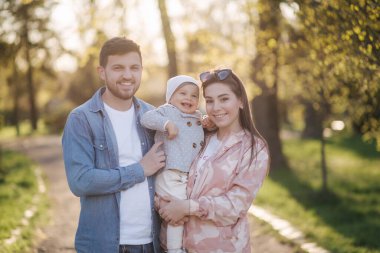Parktaki mutlu aile portresi. Baba, anne ve küçük kız. Anne ve babasıyla çok sevimli. Genç bir aile, yakışıklı bir baba ve çekici genç bir anne. Anneler Günün kutlu olsun.