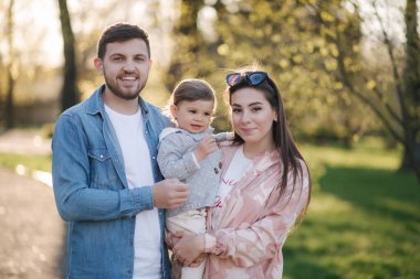 Parktaki mutlu aile portresi. Baba, anne ve küçük kız. Anne ve babasıyla çok sevimli. Genç bir aile, yakışıklı bir baba ve çekici genç bir anne. Anneler Günün kutlu olsun.