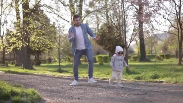 La adorable pequeña Gilr pasa tiempo con su padre. Papá y su hija caminan por el parque. Una familia con estilo. Niña feliz con gafas de sol. Papá y su hija bailan en el parque — Vídeos de Stock