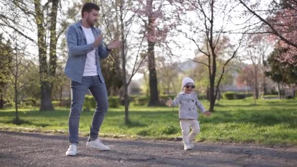 Küçük sevimli Gilr babasıyla vakit geçiriyor. Baba ve kızı parkta yürüyor. Şık bir aile. Güneş gözlüklü mutlu küçük kız. Baba ve kızı parkta dans ediyor. — Stok video