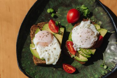 Evde nefis bir kahvaltı. Çavdar ekmeğinin üstünde taze kesilmiş avokado, kiraz domatesli ekmek ve yeşil tabakta haşlanmış yumurta. Üst görünüm