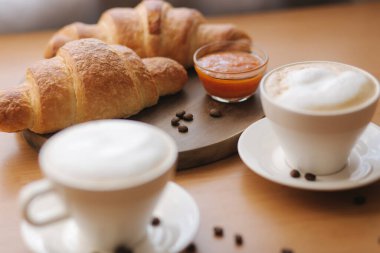 Sabah kahvesi ve kruvasan. Kapuçino ve taze pişmiş Criossant. Tahtaya boş kruvasan. Kayısı reçeli