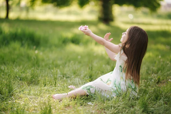 Портрет чарівної дівчинки сидить босоніж на траві в парку. Щаслива дитина на свіжому повітрі. Кінець карантину. Красива сукня — стокове фото