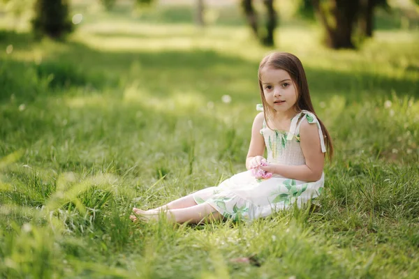 Портрет чарівної дівчинки сидить босоніж на траві в парку. Щаслива дитина на свіжому повітрі — стокове фото