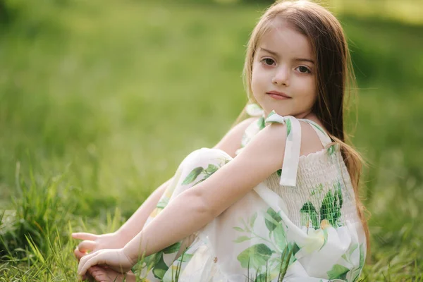 Portret van een schattig klein meisje zit blootsvoets op het gras in het park. Gelukkig kind op de frisse lucht — Stockfoto