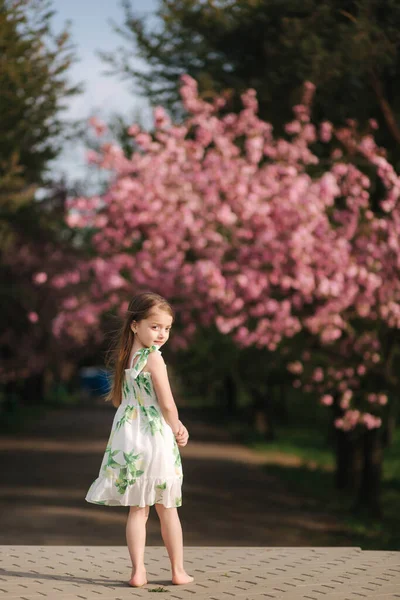 Щаслива дівчинка гуляє босоніж в парку, на фоні рожевого дерева сакури. Кінець карантину. мила дівчинка — стокове фото