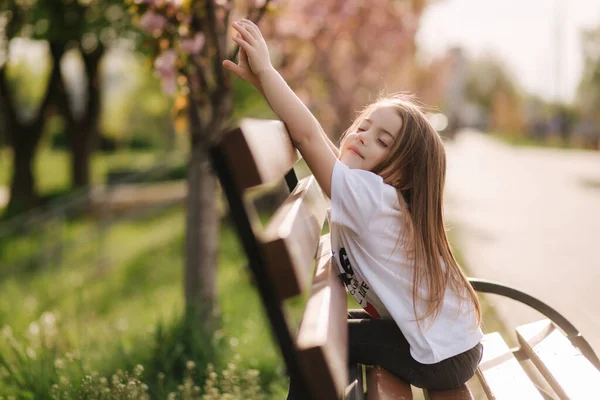 Счастливая девочка сидит на скамейке в парке. Свежий воздух. Конец карантина — стоковое фото