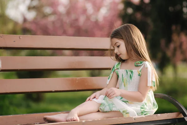Счастливая девочка сидит на скамейке в парке. Красивое летнее платье. Свежий воздух. Конец карантина — стоковое фото