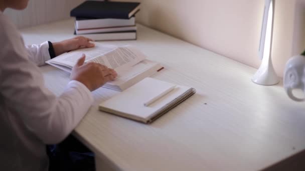 Młody chłopak siedzi przy biurku i czyta książkę w notatniku. Badanie w domu podczas kwarantanny — Wideo stockowe