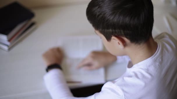 Jonge jongen aan het bureau las het boek en schreef het op in het notitieboekje. Studeer thuis tijdens quarantaine. Afstandsonderwijs — Stockvideo