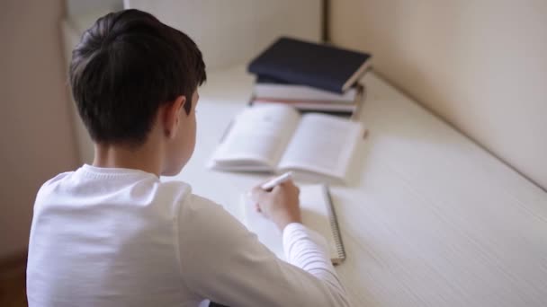 Young boy sitting at desk read the book and write down in notebook. Study at home during quarantine. Distance learning — Stock Video