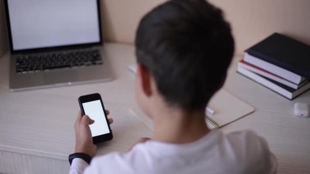 Ο μαθητής σπουδάζει στο γραφείο του στο δωμάτιό του. Αγόρι χρήση φορητού υπολογιστή και smartphone για να γράψετε στο σημειωματάριο. Βιβλία και τάμπλετ στο τραπέζι. Μελέτη στο σπίτι κατά τη διάρκεια της Qurantine — Αρχείο Βίντεο