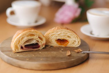 Ahşap tahtada farklı reçelli iki parça taze çıplak kruvasan. Cappuccino 'nun arka planı