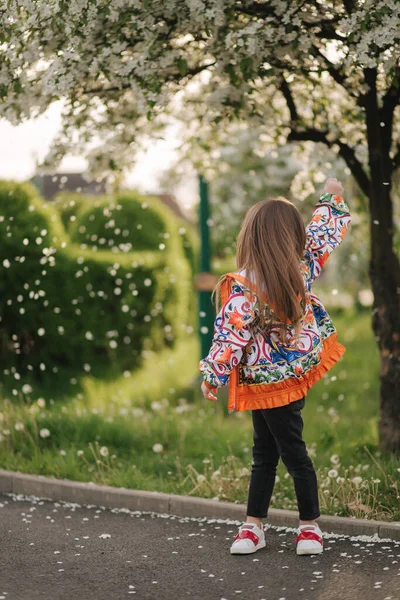 Мила маленька дівчинка стоїть перед квітковим деревом. Пелюстки дме, як сніг. Красиве біле квітуче дерево — стокове фото