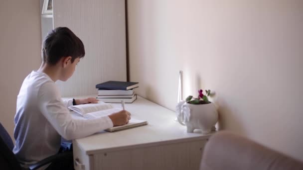 Ein kleiner Junge sitzt am Schreibtisch und liest das Buch. Während der Quarantäne zu Hause studieren — Stockvideo