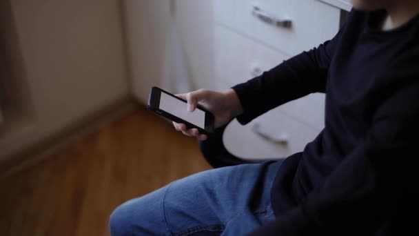 El colegial en el hogar usa el teléfono inteligente durante el descanso. Estudia en casa. Feliz joven sonrisa — Vídeos de Stock