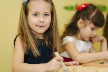 Sınıftaki çocuklar kumla çizim yaparlar. Çocuklar doğramak için püskül kullanırlar. Anaokulu