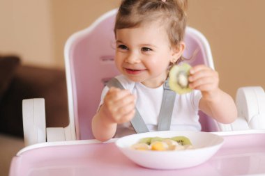 Yüksek sandalyede kivi yiyen mutlu küçük çocuk portresi. Çocuklar için sağlıklı beslenme