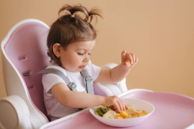 Yüksek sandalyede egzotik meyveler yiyen mutlu genç kızın portresi.