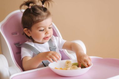 Yüksek sandalyede egzotik meyveler yiyen mutlu genç bir kızın portresi. Çocuklar için sağlıklı beslenme