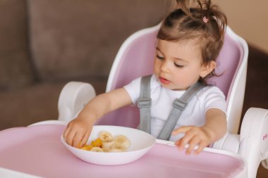Yüksek sandalyede egzotik meyveler yiyen mutlu genç bir kızın portresi. Çocuklar için sağlıklı beslenme