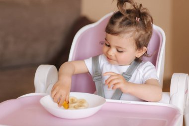 Yüksek sandalyede egzotik meyveler yiyen mutlu genç bir kızın portresi. Çocuklar için sağlıklı beslenme