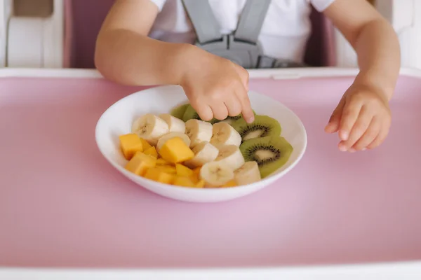 Közelkép a kislány, hogy egzotikus gyümölcsöt tányér etetőszék. Szeletelt mangó, kivi és banán — Stock Fotó