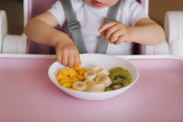 Közelkép a kislány, hogy egzotikus gyümölcsöt tányér etetőszék. Szeletelt mangó, kivi és banán — Stock Fotó