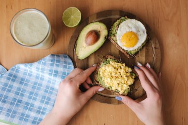Avokado sandviçinde farklı pişmiş yumurta ve tahtadan yapılmış tahtadan yapılmış tam tahıllı ekmek. Ispanaklı meyve püresi. Üst Manzara. Vejetaryen gıda konsepti
